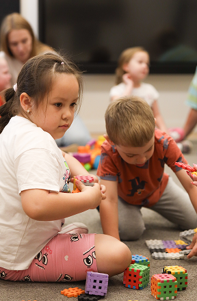 Dzieci siedzą na podłodze i bawią się kolorowymi plastikowymi klockami w klasie.