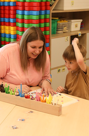 Kobieta i chłopiec siedzą przy stole z kolorowymi kredkami i papierem, angażując się we wspólne zajęcia w klasie.